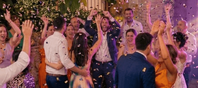 A wedding dancefloor mid-celebration, hands in the air under confetti